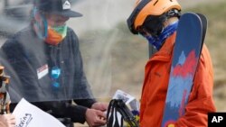 FILE - An employee is protected by a plexiglass shield while processing a skier at the reopening of Arapahoe Basin Ski Resort, which closed in mid-March to help in the effort to stop the spread of the new coronavirus.