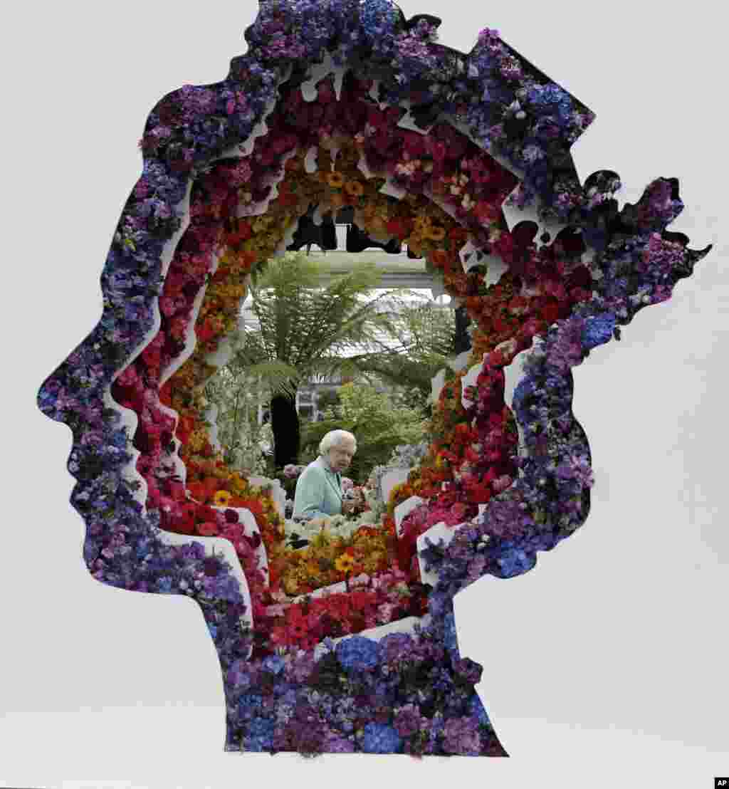 Britain&#39;s Queen Elizabeth is pictured through a gap in a floral exhibit by the New Covent Garden Flower Market at the 2016 Chelsea Flower Show in central London.