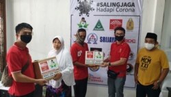 Dua orang warga menerima paket sembako yang dapat, mereka adalah warga terdampak corona yang masuk dalam pekerja informal. (Foto: VOA/Petrus Riski)