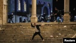 A Palestinian hurls stones at Israeli police during clashes at the compound that houses Al-Aqsa Mosque amid tension over the possible eviction of several Palestinian families, May 7, 2021.