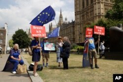 FILE - Anti-Brexit, EU supporters hold placards and European Union flags on Abingdon Green, backdropped by the Houses of Parliament in London, July 9, 2018.