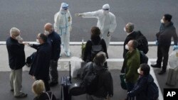 A worker in protective coverings directs members of the World Health Organization (WHO) team on their arrival at the airport in Wuhan in central China's Hubei province on Thursday, Jan. 14, 2021. (AP Photo/Ng Han Guan)