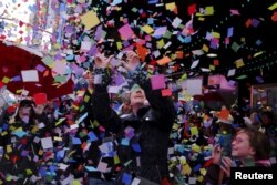 FILE - Pedestrians watch confetti fall as members of the Times Square Alliance perform an "air worthiness test" for the confetti that is similar to what will be used for New Year's Eve in New York on Dec. 29, 2015.