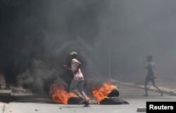 Somali demonstrators run past burning tires during protests sparked by the killing of a rickshaw driver and passenger in Mogadishu, Somalia, April 13, 2019.