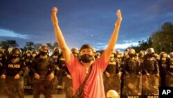 រូបឯកសារ៖ បាតុករ​ថៃ​ម្នាក់​លើកដៃ​ឡើង ខណៈ​ដែល​ប៉ូលិស​ឈរ​យាម​ល្បាត​នៅ​ពី​ក្រោយ នៅ​ក្បែរ​អគារ​រដ្ឋាភិបាល ក្នុង​អំឡុងពេល​នៃ​ការ​ធ្វើ​បាតុកម្ម​មួយ ក្នុង​ទីក្រុង​បាងកក ប្រទេស​ថៃ ថ្ងៃទី២៤ ខែមិថុនា ឆ្នាំ២០២១។