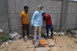 The caretaker of a crematorium, center, tries to console a man who lost his 5-month-old child to COVID-19 as they perform a post-burial ritual at the Seemapuri crematorium in New Delhi, India, May 13, 2021.