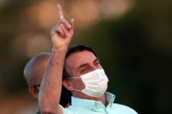 FILE - Brazil's President Jair Bolsonaro, who is infected with COVID-19, wears a protective face mask as he attends a Brazilian flag retreat ceremony outside his official residence the Alvorada Palace, in Brasilia, Brazil, July 22, 2020.