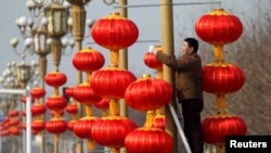 Seorang pria menggantung lentera di pinggir jalan di Xuchang, provinsi Henan, China, menjelang Tahun Baru China (15/1). 