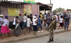 FILE - A member of the South African National Defense Force keeps watch as shoppers leave a grocery store, after being ordered by law enforcement during a lockdown to contain the coronavirus disease, in Alexandra, South Africa, March 27, 2020.