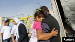 Seorang pria menggendong putrinya melintasi rumah warga sipil yang hancur akibat serangan mortir di wilayah pemukiman Akcakale, Turki (4/10). Lima orang dikabarkan tewas dalam insiden tersebut.