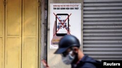 FILE - A man uses a smartphone as he walks past a poster warning against the spread of 'fake news' on the coronavirus, in Hanoi, Vietnam April 14, 2020. 