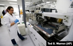 Caitlin Cramer, a PhD student in materials science engineering, demonstrates a machine that can produce electrical circuits and solar cells at the newly opened Washington Clean Energy Testbeds laboratory housed in the University of Washington.