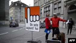 Orang-orang berdiri di papan bertuliskan "Kami memilih hari ini" dalam bahasa Perancis di kota tua Fribourg, Swiss, 30 November 2014. 