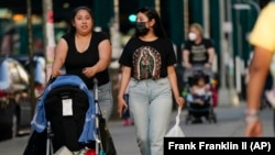 Two women -- one with a mask, one without -- walk along Roosevelt Avenue in the Queens borough of New York, May 19, 2021. (AP Photo/Frank Franklin II)