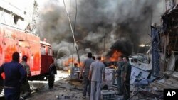 Quelques personnes se rassemblent autour des bâtiments en feu après une attaque à la bombe dans la banlieue de Sayyida Zeinab, à Damas, Syrie, 11 juin, 2016. (SANA via AP)