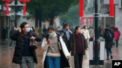 Masked pedestrians walk down a shopping street in downtown Wuhan, China, Jan. 22, 2020. 