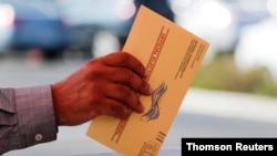 FILE PHOTO: An election worker places a mail-in ballot into an election box at a drive-through drop off location at the Registrar of Voters in San Diego, California