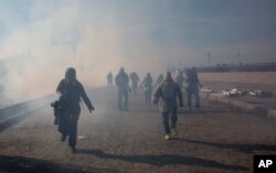 Migrants run from tear gas launched by U.S. agents, amid photojournalists covering the Mexico-U.S. border, after a group of migrants got past Mexican police at the Chaparral crossing in Tijuana, Mexico, Sunday, Nov. 25, 2018.