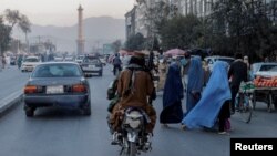  اعضای مسلح طالبان با موتورسیکلت از کنار چند زن که برقع پوشیده‌اند در خیابانی در کابل عبور می‌کنند (آرشیو)