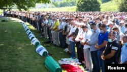People pray near coffins at a graveyard during a mass funeral in Potocari near Srebrenica, Bosnia and Herzegovina July 11, 2020.