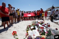 FILE - People, some displaying a Tunisian flag, stand in silence next to flowers during a gathering at the scene of the attack in Sousse, Tunisia, June 28, 2015.