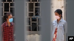 FILE: Women is masks watch employees of the non-profit Cambodian Children's Fund spray disinfectant in help curb the spread of the new coronavirus in the slum neighborhood of Stung Meanchey in southern Phnom Penh, Cambodia, on Tuesday, March 24, 2020. (AP Photo/Heng Sinith) 