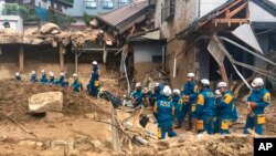 Emergency teams rest outside building with structural damage caused by heavy rains, July 9, 2018, in Hiroshima, Japan. 