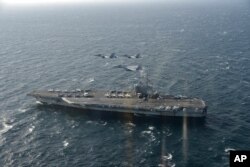 In this Nov. 10, 2017, photo provided by Japan's Air Self-Defense Force, two U.S. F/A-18s and Japanese F-15s fly over the USS Ronald Reagan toward a joint military exercise at an undisclosed location.