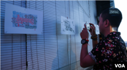 យុវជន​មួយ​រូប ថតរូប​គំនូរ​ដែល​ត្រូវ​បាន​ដាក់​តាំង​ក្នុង​ការតាំង​ពិព័រណ៍​ដែល​ត្រូវ​បាន​រៀបចំ​ឡើង​នៅ​រាជធានី​ភ្នំពេញ​កាលពី​ថ្ងៃ​ទី២១ ខែមីនា កន្លង​ទៅ​នេះ។ (ឡេង ឡែន/VOA)