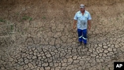 FILE - A farmer stands on cracked earth that three weeks earlier created the bottom of a reservoir on his farm, in Groot Marico, South Africa, Nov. 12, 2015. 