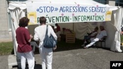 FILE - Two women stand in front of an information stand raising awareness against sexual assault and street harassment during the 81st Bayonne Festival (Fetes de Bayonne) in Bayonne, southwestern France, July 27, 2017.