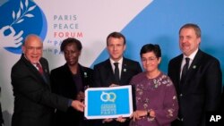 French President Emmanuel Macron, center, OECD secretary-general Angel Gurria, left, and U.N officers hold a placard as part of a move to promote gender equality at the Paris Peace Forum, Nov. 12, 2019. 