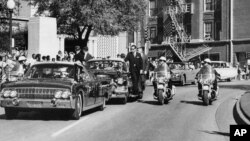 FILE - In this Nov. 22, 1963, photo, President John F. Kennedy's hand, visible through the foreground convertible's windshield, reaches toward his head within seconds of the firing of the fatal shot as first lady Jacqueline Kennedy holds his forearm, with the motorcade proceeding along Elm Street past the Texas School Book Depository in Dallas.