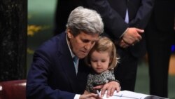 FILE - Then-U.S. Secretary of State John Kerry holding his granddaughter, Isabelle Dobbs-Higginson, signs the book during the signature ceremony for the Paris Agreement at the United Nations General Assembly Hall, April 22, 2016, in New York.