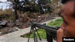 Seorang polisi Myanmar siaga di dekat kawasan permukiman yang dibakar dalam kekerasan di kota Maungdaw, negara bagian Rakhine, Myanmar (30/8).