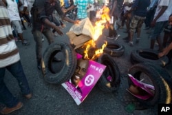 Supporters of presidential candidate Maryse Narcisse, from the Fanmi Lavalas political party, burn tires and a campaign poster of rival candidate Jovenel Moise, from the PHTK party, in Port-au-Prince, Haiti, Nov. 28, 2016.