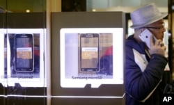 FILE - A man uses an Apple iPhone as he passes a Samsung shop in Seoul, South Korea, Jan. 29, 2015.