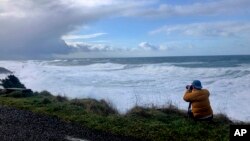 In this Jan. 11, 2020 photo a man photographs waves crashing onto the cliffs at Rodea Point in Lincoln County, Oregon, during an extreme high tide that happened during a big winter storm. (AP Photo/Gillian Flaccus)