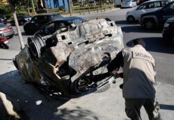 A private security worker photgraphs a car burned by supporters of the Shiite Hezbollah and Amal groups in Beirut, Dec. 17, 2019. The groups were angered by a video that showed a man insulting Shiite figures.