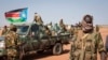 A South Sudanese government soldier stands with others near their vehicles, after government forces on Friday retook from rebel forces the provincial capital of Bentiu, in Unity State, South Sudan, Sunday, Jan 12, 2014.