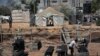 FILE - Two Palestinian boys stand outside a tent, background, watching workers rebuild a house which was destroyed during the 2014 summer war between Israel and Hamas, as the long-awaited reconstruction began in Shijaiyah neighborhood eastern Gaza City, July 23, 2015.