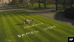 In this image from VTM video, Belgium's King Philippe, right, stands with members of his family in the Royal Gardens of Laeken with a message 'Courage, strong together' written on the lawn on April 4, 2020. (VTM via AP)