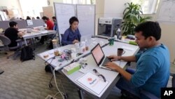 In this Thursday, June 30, 2016 photo, Babson College graduate school alumnus Abhinav Sureka, of Mumbai, India, right, types in his work space at the college in Wellesley, Mass.