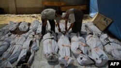 FILE - A Syrian emergency personnel and a civilian inspect the bodies of Syrian men outside a makeshift hospital in a rebel-held area of Douma, east of the capital Damascus, Aug. 12, 2015.