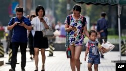 Para pejalan kaki memeriksa telepon pintarnya sembar berjalan di trotoar di Beijing, 9 Agustus 2017.