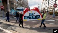 FILE - Sammi LeMaster, left, and Katherine Fuchs, right, carry the top of an alarm clock display that reads "Net Neutrality" down 12th Street SW to their truck after a protest at the Federal Communications Commission (FCC) in Washington, Thursday, Dec. 14, 2017. (AP Photo/Carolyn Kaster)