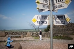 Tourists pose for photograph next to a mock road sign for Damascus, the capital of Syria, and other capitals and cities, in an old outpost in the Golan Heights near the border with Syria, March 22, 2019.