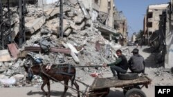 Palestinian boys ride a donkey-pulled cart near a building destroyed in Israeli bombardment in Rafah in the southern Gaza Strip on March 31, 2024.