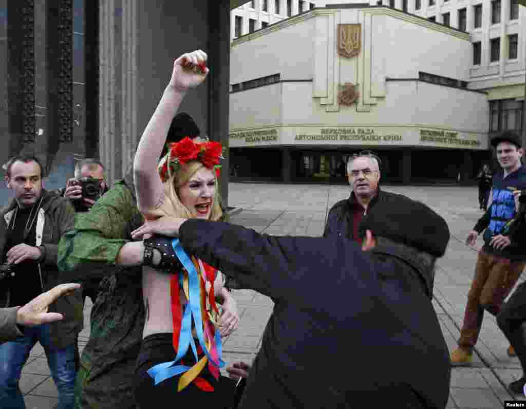 Members of Crimean self-defence units block a topless activist from the Ukrainian feminist group Femen during a protest near the Crimean parliament building in Simferopol, March 6, 2014. 