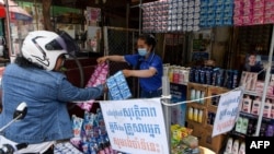 FILE - A vendor shows sachets of hair shampoo to a customer from a shop that has been marked off to allow for social distancing, as a preventive measure against the spread of the COVID-19 novel coronavirus, in Phnom Penh, May 27, 2020. 